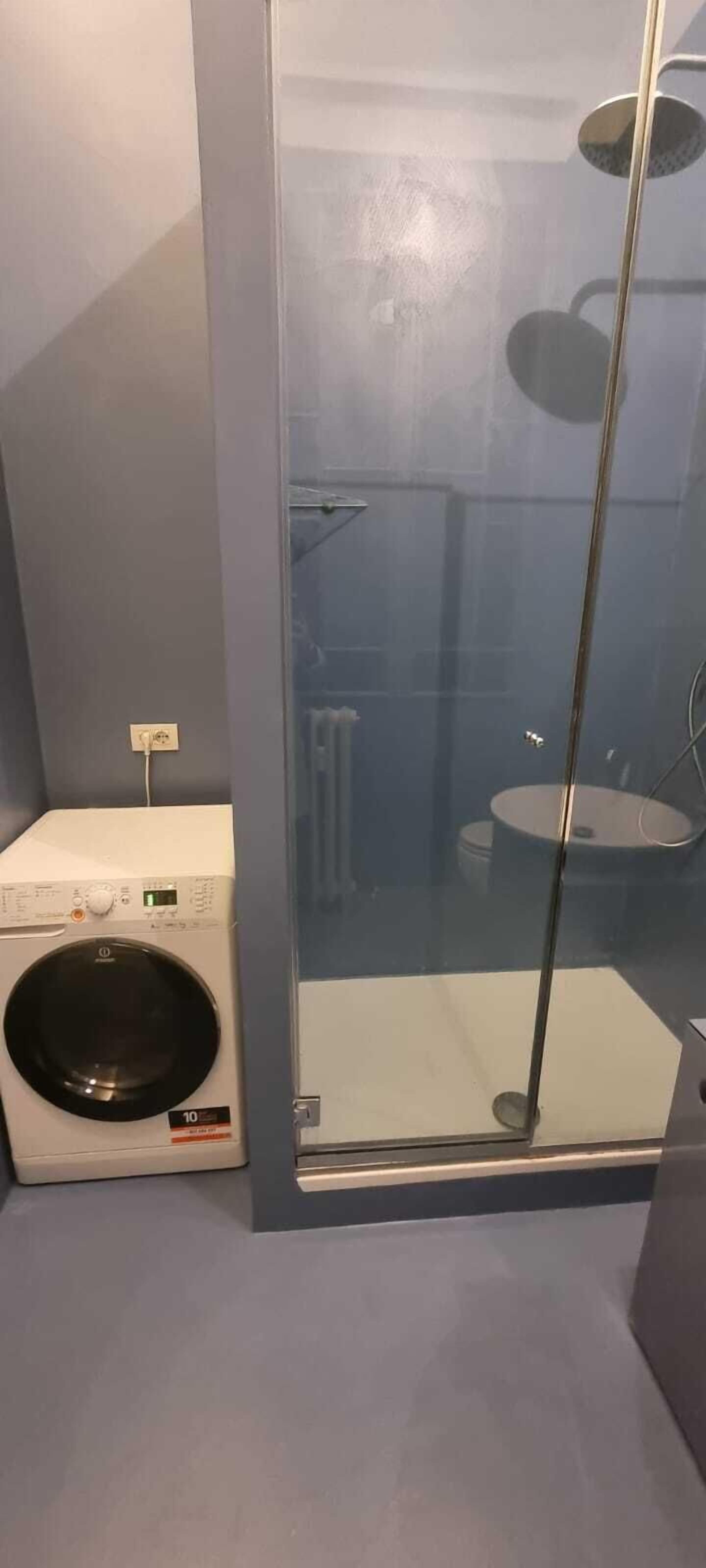 Een kleine badkamer met een douchecabine van glas, een wasmachine en een toilet.