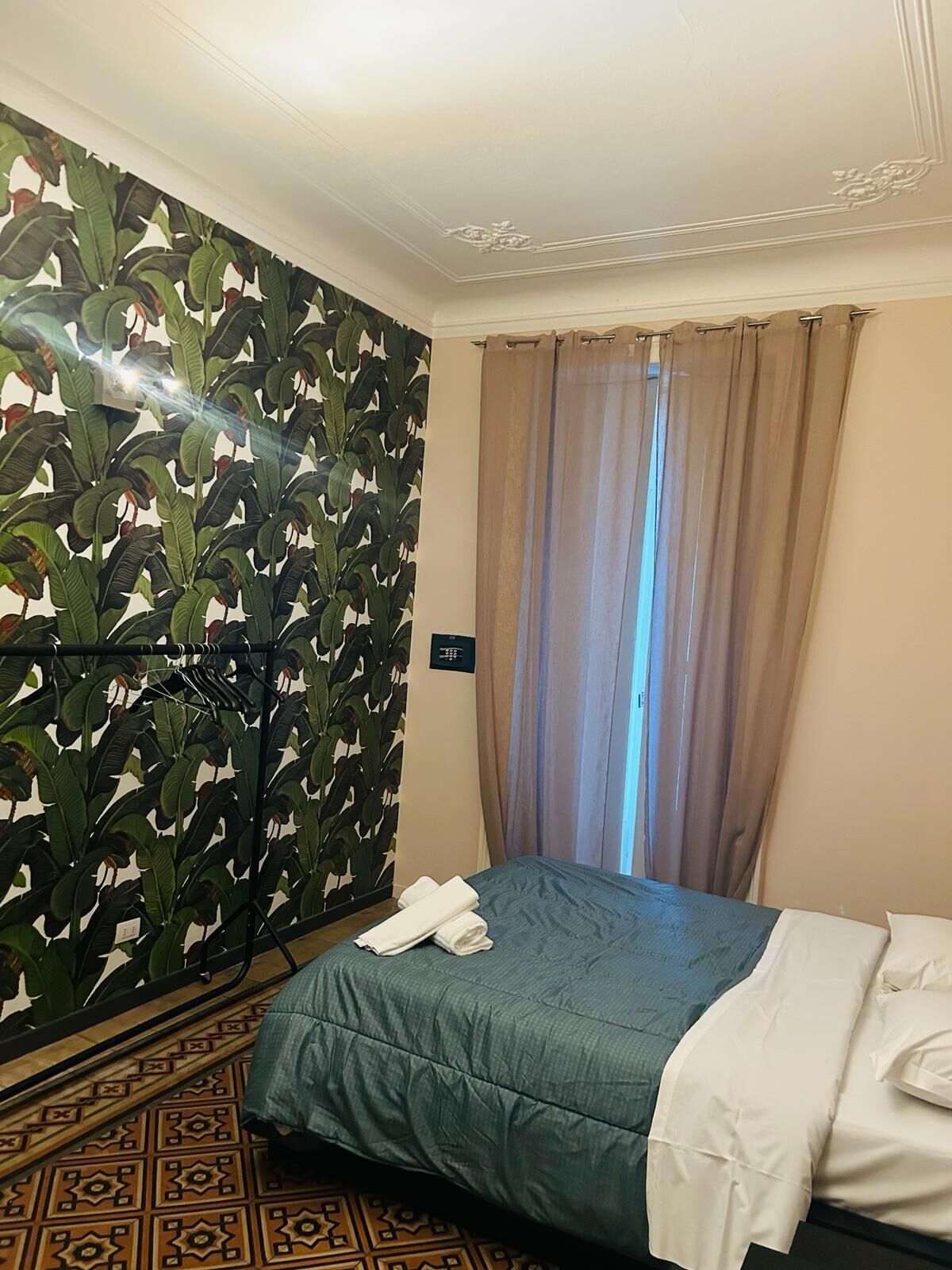 Ein Hotelzimmer mit Bett, Vorhang und Wand mit Pflanzenmuster.