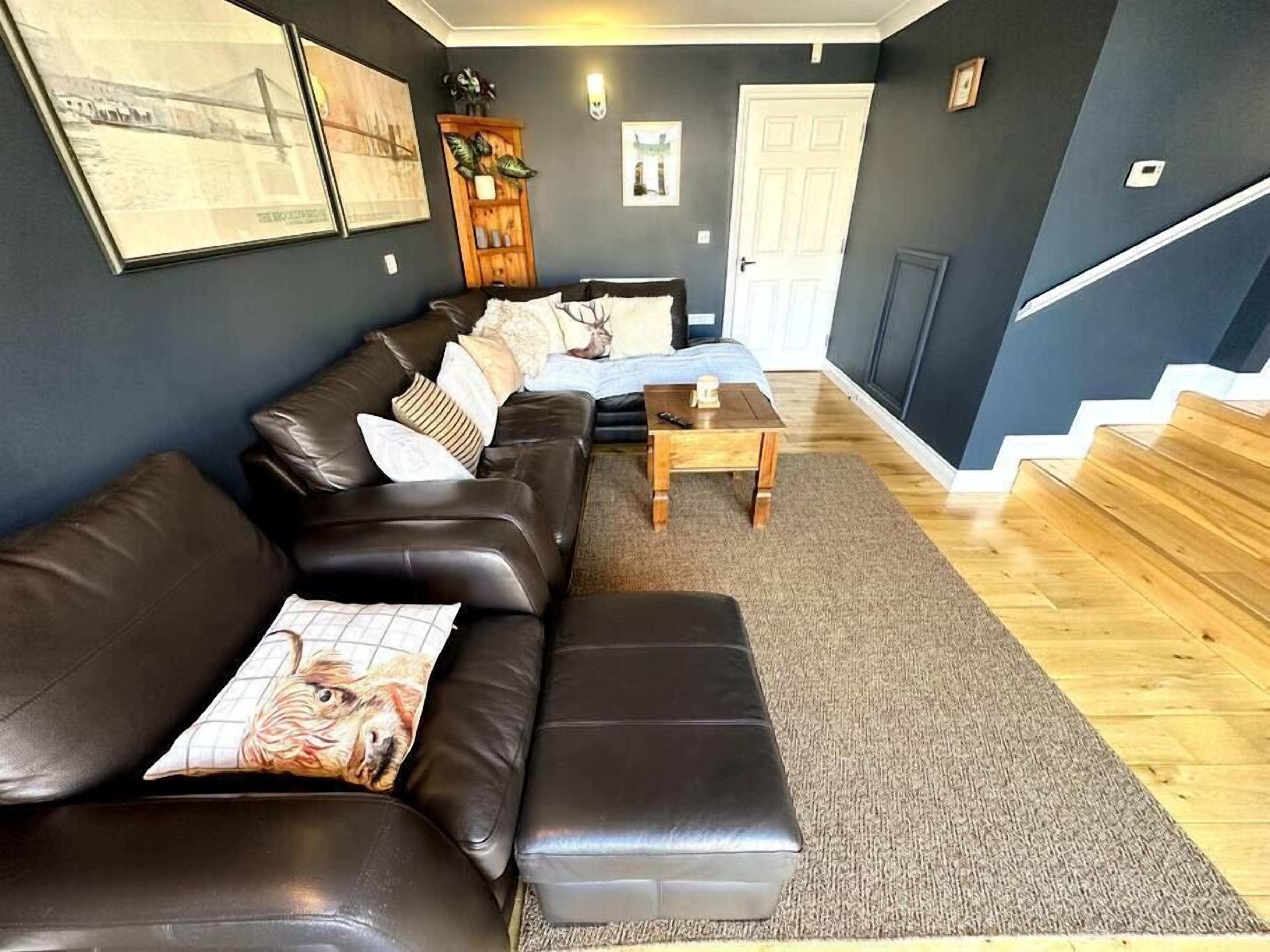 A living room with a dark blue wall, a brown leather sofa, a wooden coffee table, and a staircase.