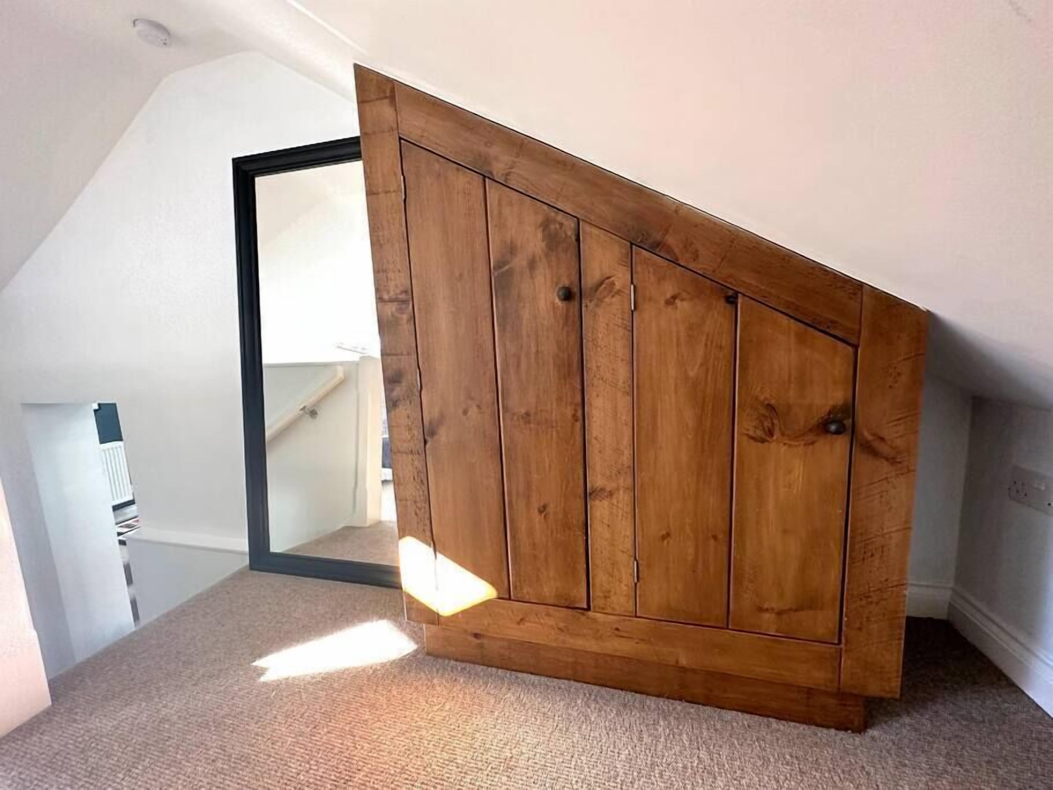 Ein Zimmer mit schrägverdeckter Decke, einem Holzschrank und einem Teppichboden.