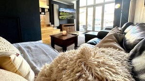 A modern living room with a sofa, a coffee table, and a TV. There is a large window with a view of the outside. - 2 Car Parking Spaces, Pet Friendly, Central Bakewell In The Peak District (Bakewell)