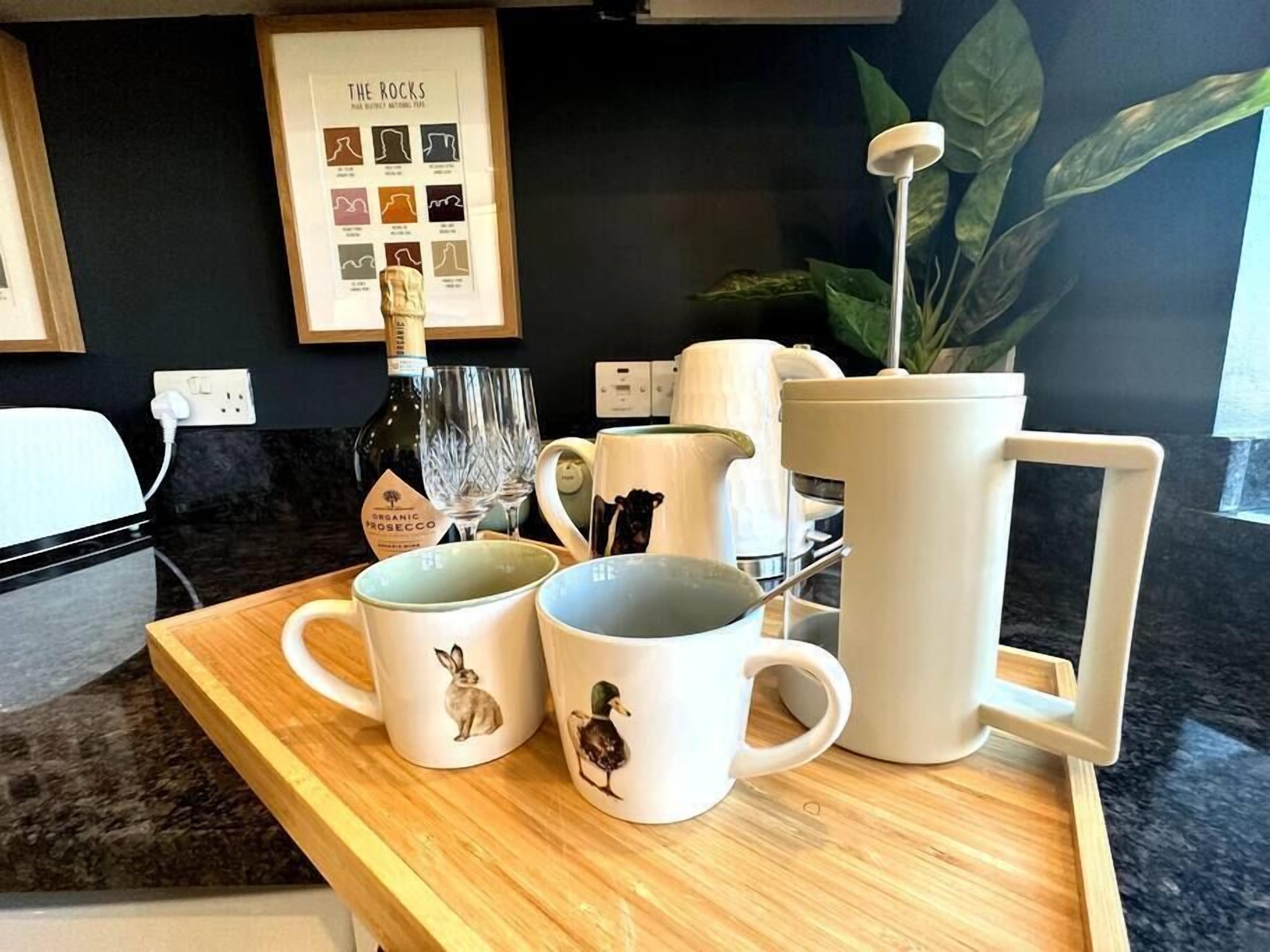 Un bancone cucina con una macchina del caffè, una bottiglia di prosecco biologico, due tazze decorate con motivi animalier e un menu incorniciato appeso al muro.