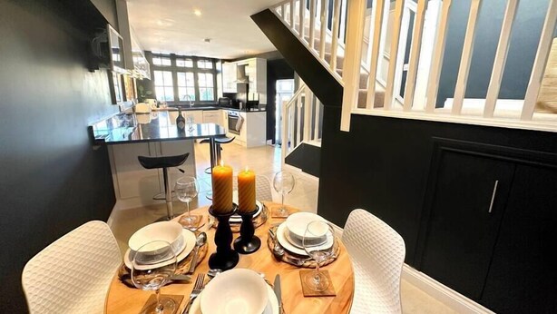 A dining area with a wooden table set for four, two candles, and a view of the kitchen and living area. - 2 Car Parking Spaces, Pet Friendly, Central Bakewell In The Peak District (Bakewell)
