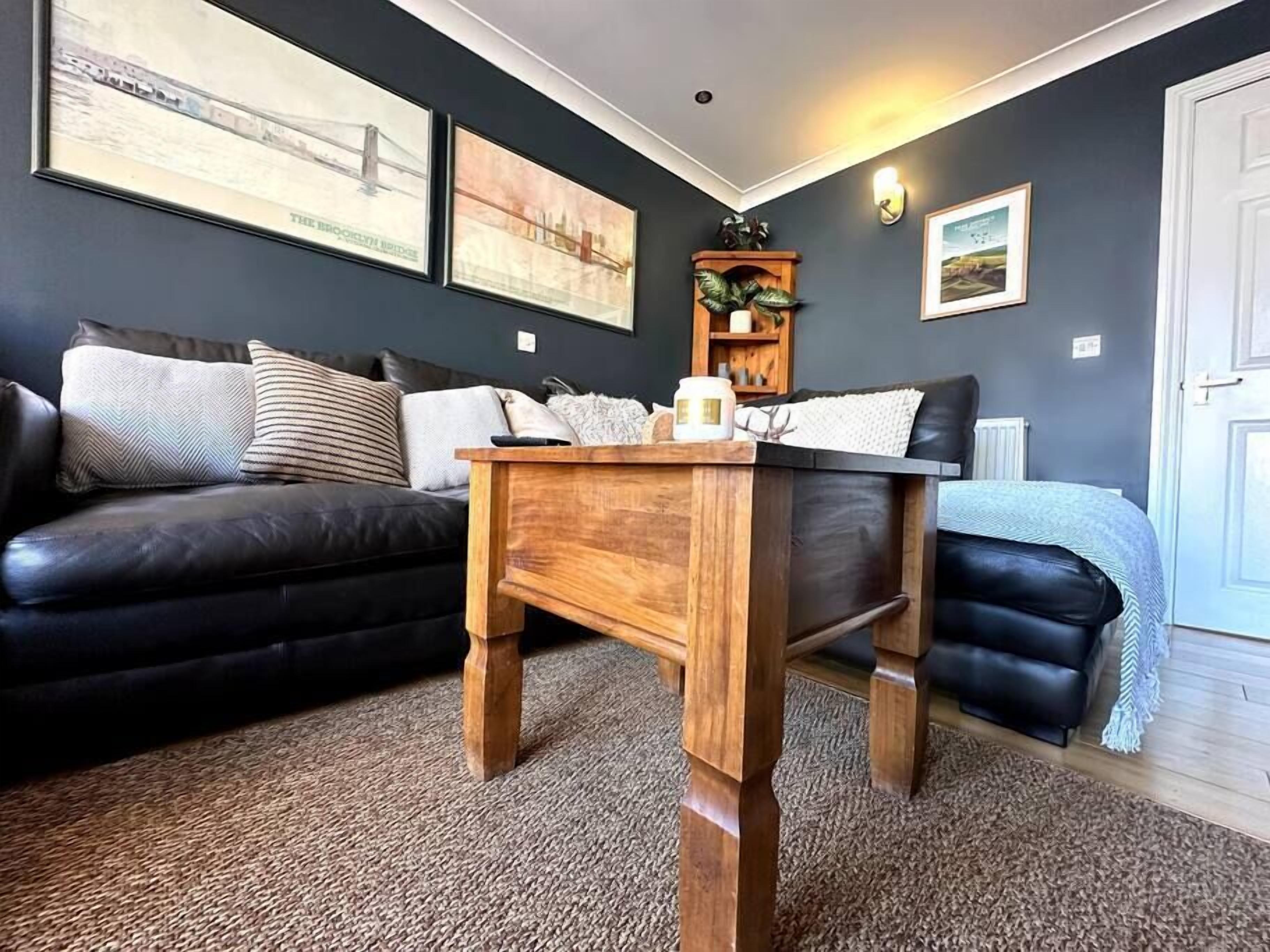 Una sala de estar con un sofá de color oscuro, una mesa de centro de madera y piso alfombrado.