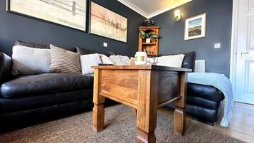 Una sala de estar con un sofá de color oscuro, una mesa de centro de madera y piso alfombrado.
