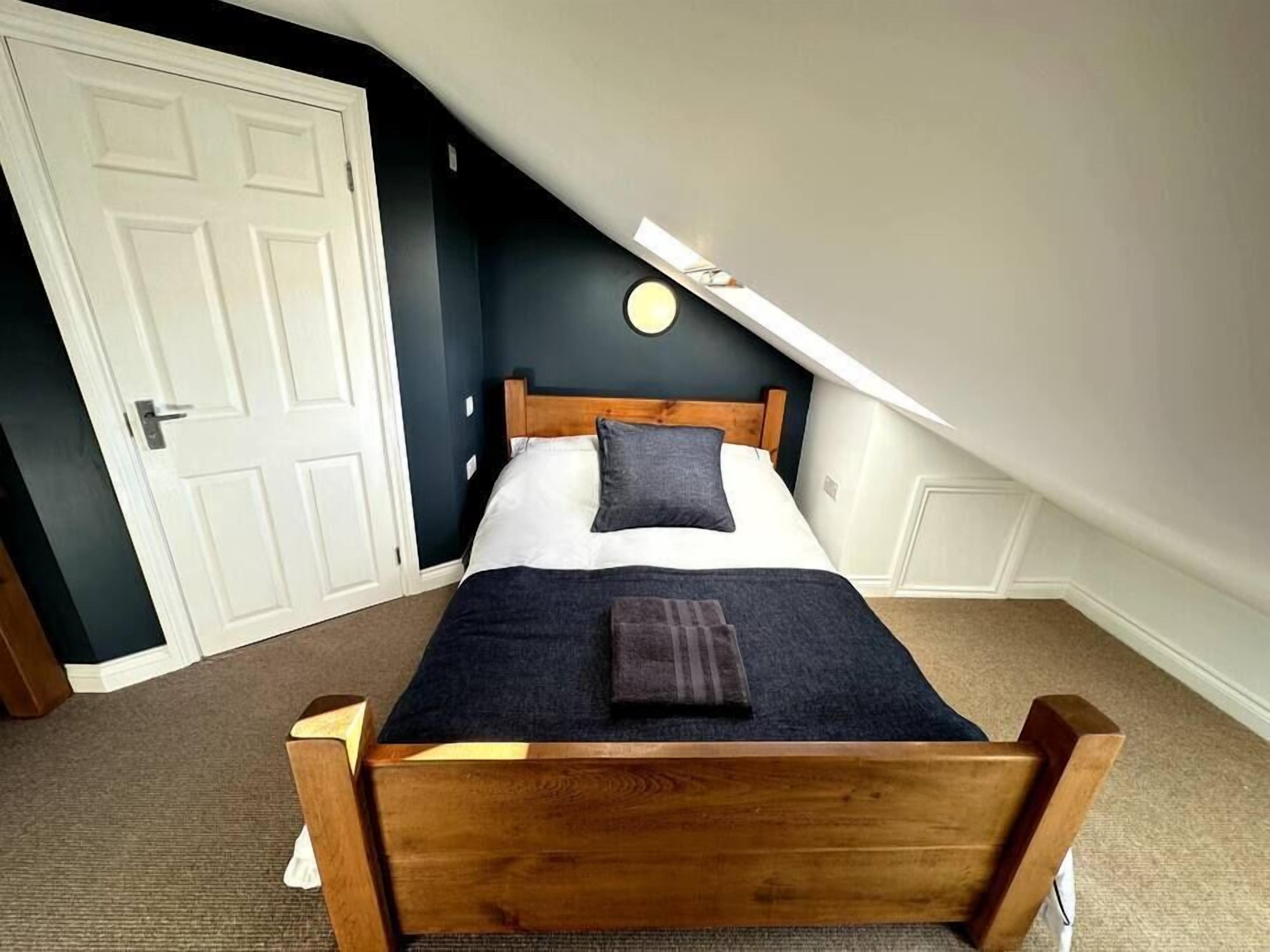 Une chambre avec un lit en bois, une porte blanche et un plafond en pente.