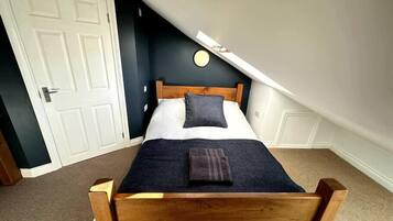 Une chambre avec un lit en bois, une porte blanche et un plafond en pente.