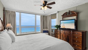 Un dormitorio con una cama grande, ventilador de techo, televisión y vista al océano.
