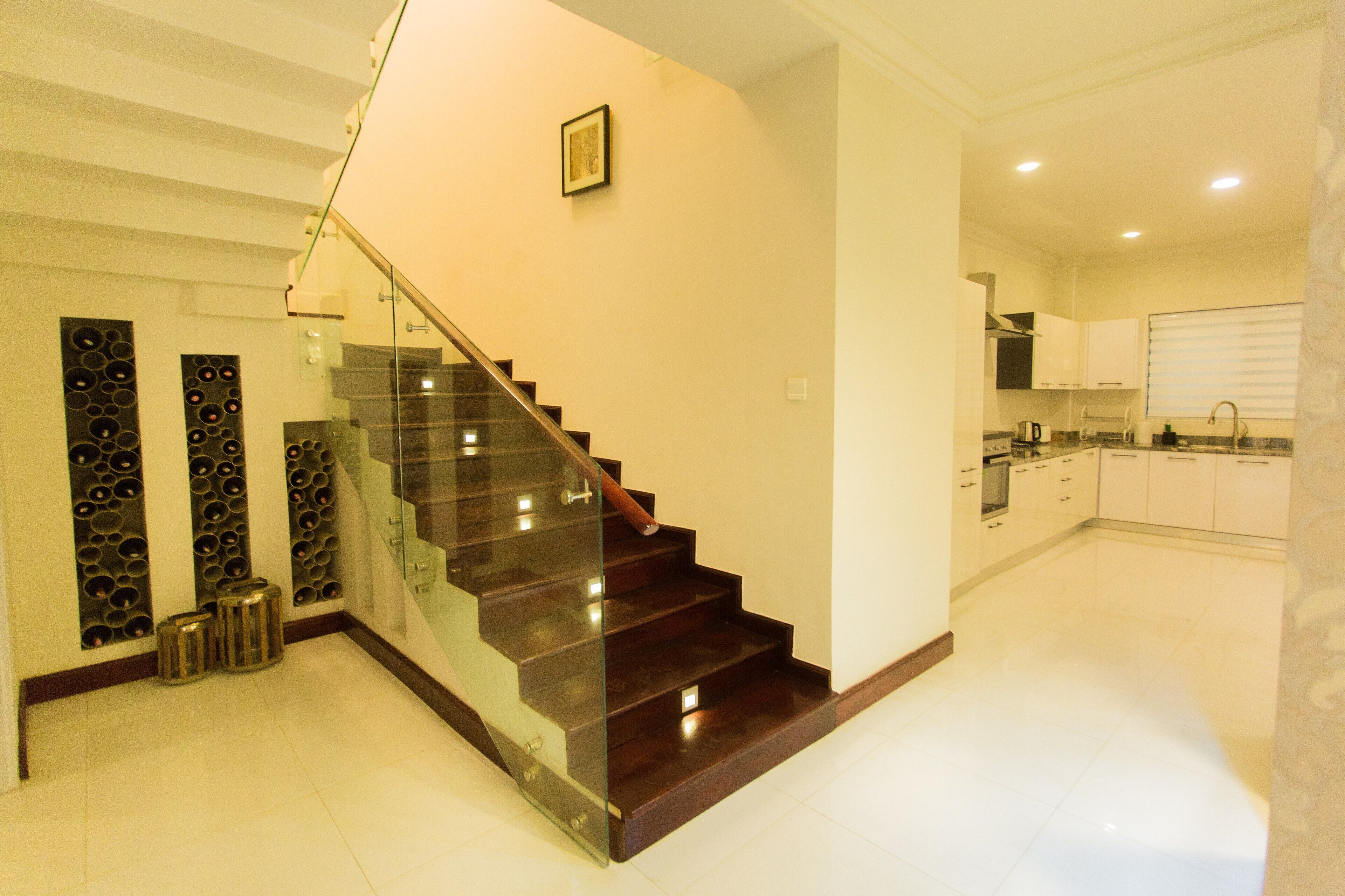 Una cocina moderna con armarios blancos, un lavamanos de acero inoxidable y una escalera de cristal que sube a otro nivel.