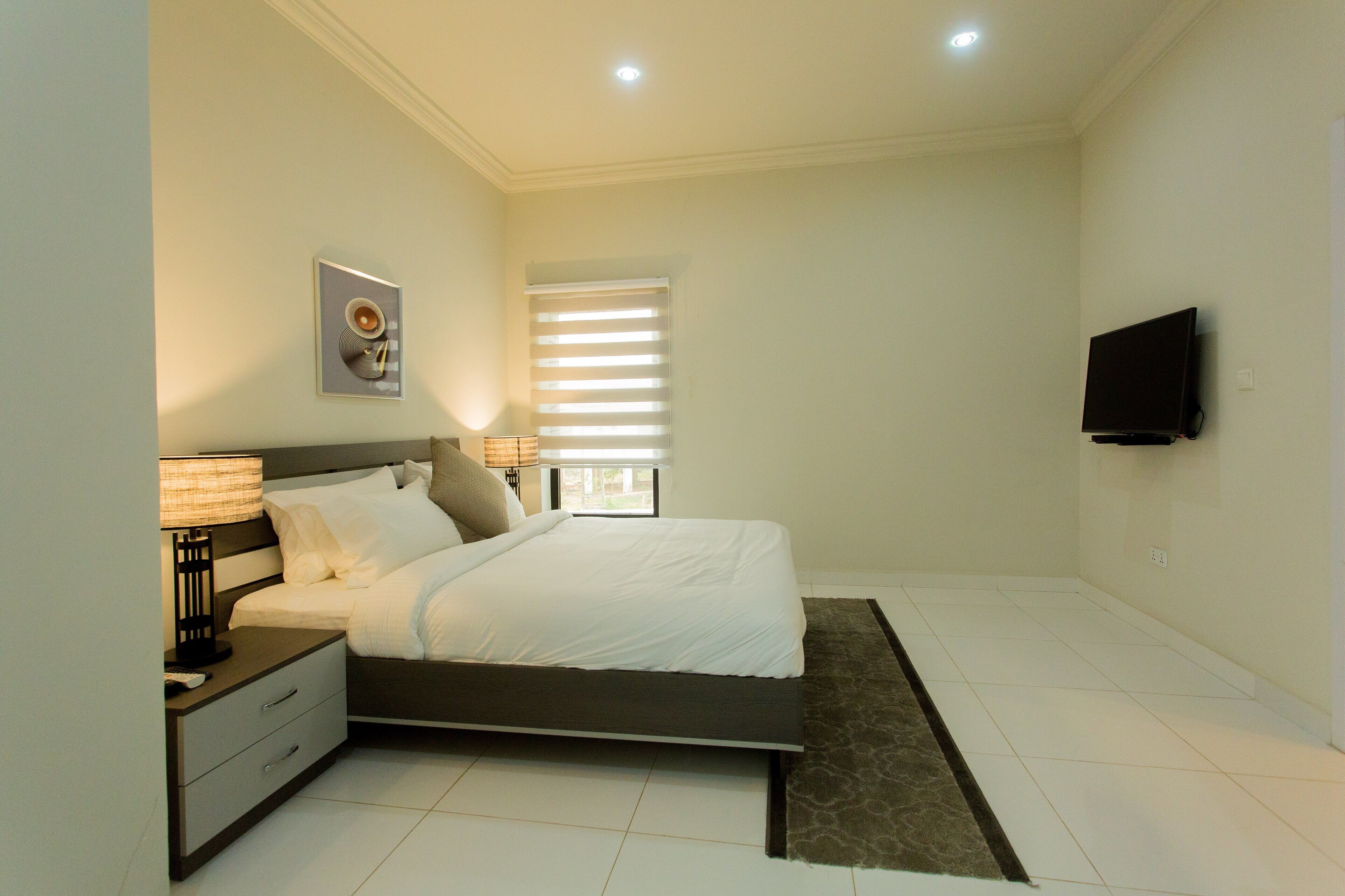 Un dormitorio moderno con cama, mesita de noche, lámpara y televisor de pantalla plana montado en la pared.