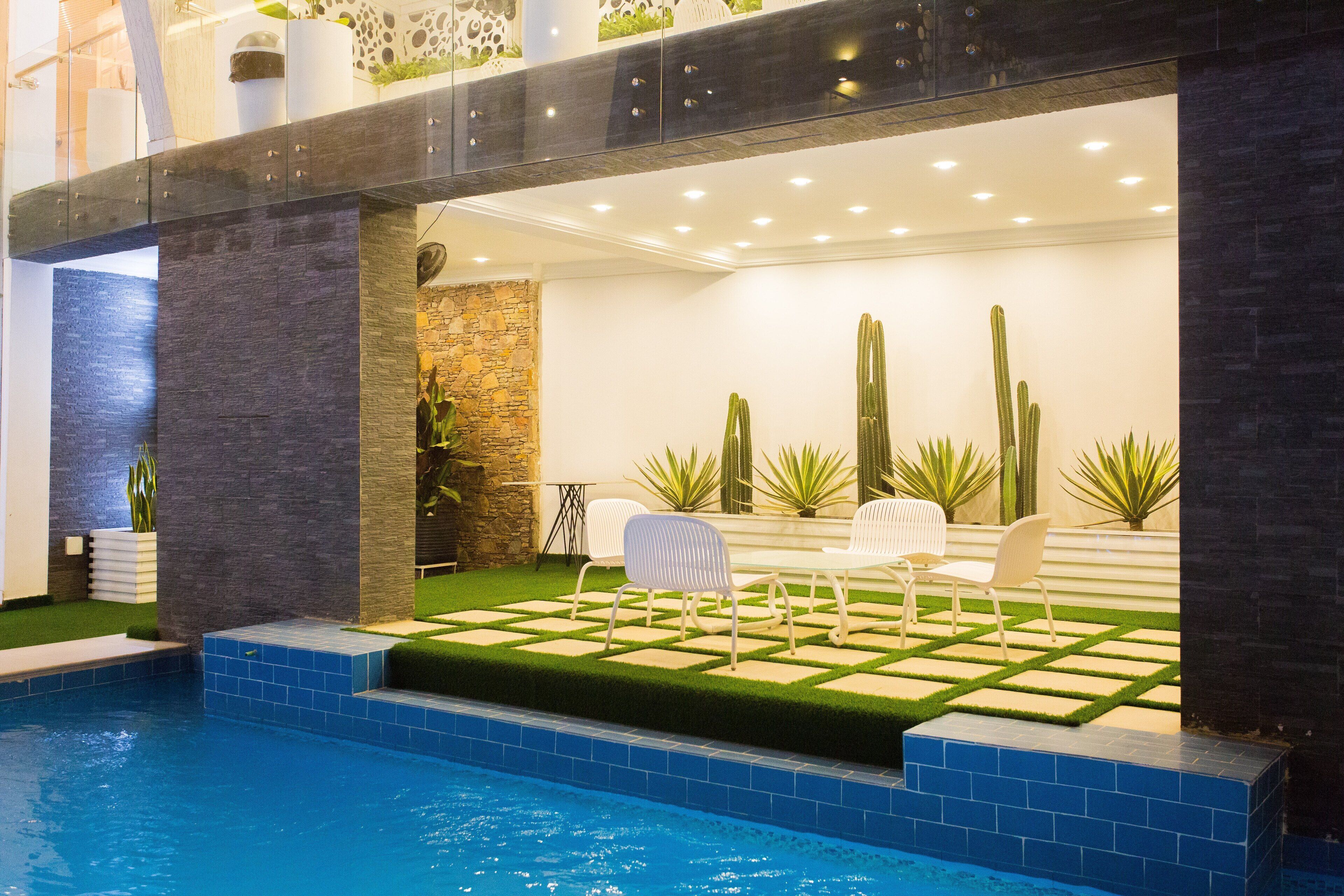 A modern pool area with a stone wall, a seating area with chairs, and cacti.