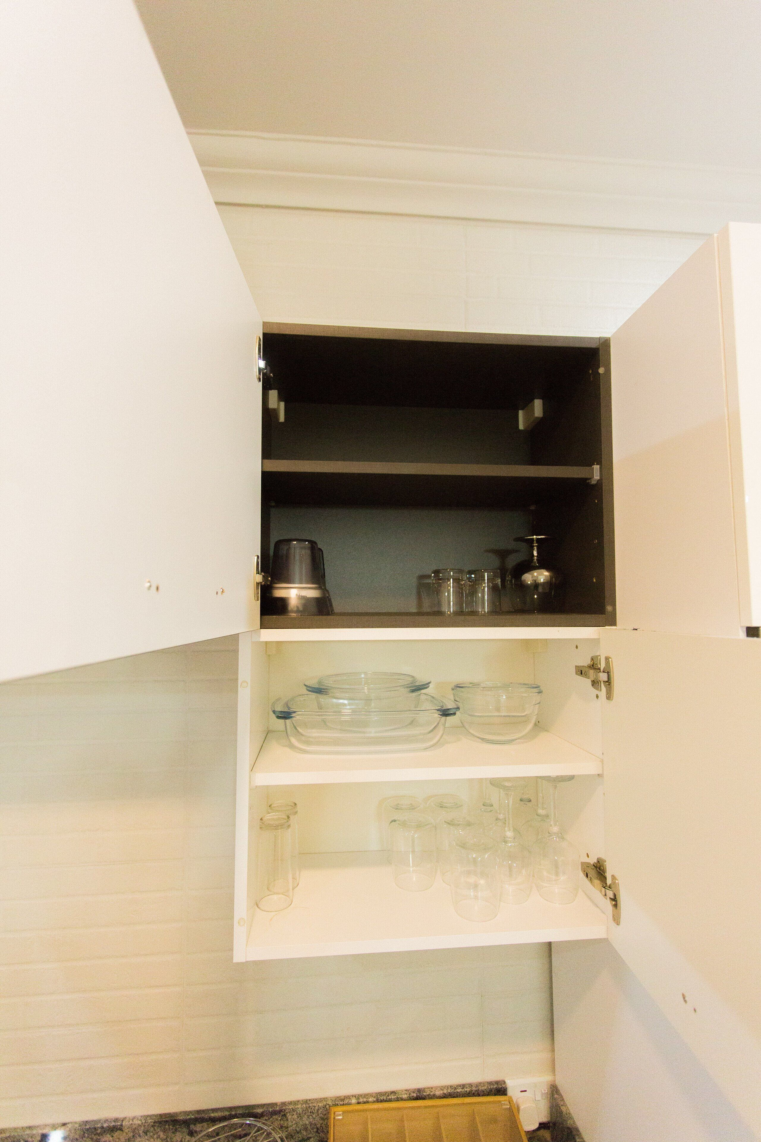 Una cocina con armarios blancos, una cafetera y cristalería.