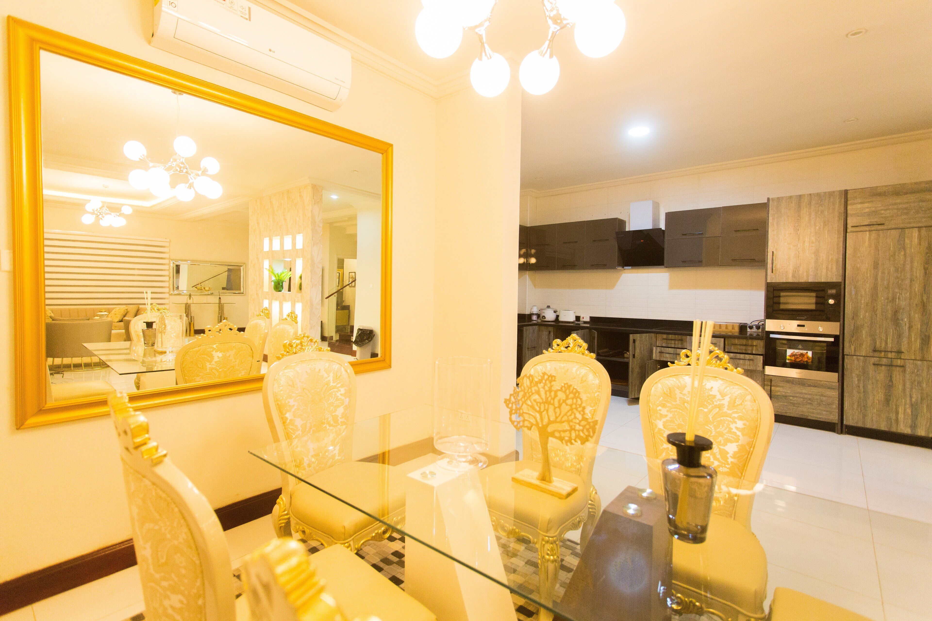 A dining area with a glass table, ornate chairs, and a large mirror.