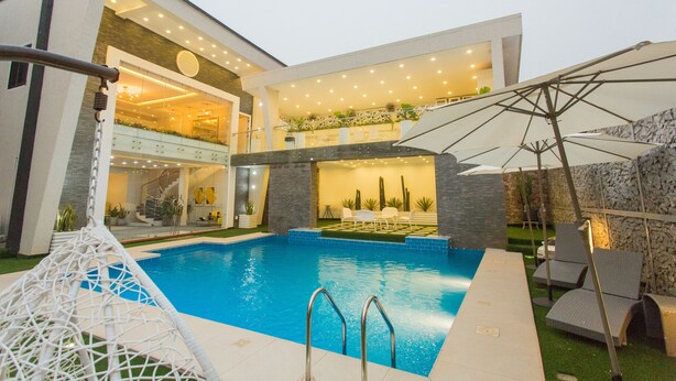 A modern house with a swimming pool, outdoor seating, and a well-lit interior. - Kumasi Luxury Apartments at The Fairview (Kumasi)