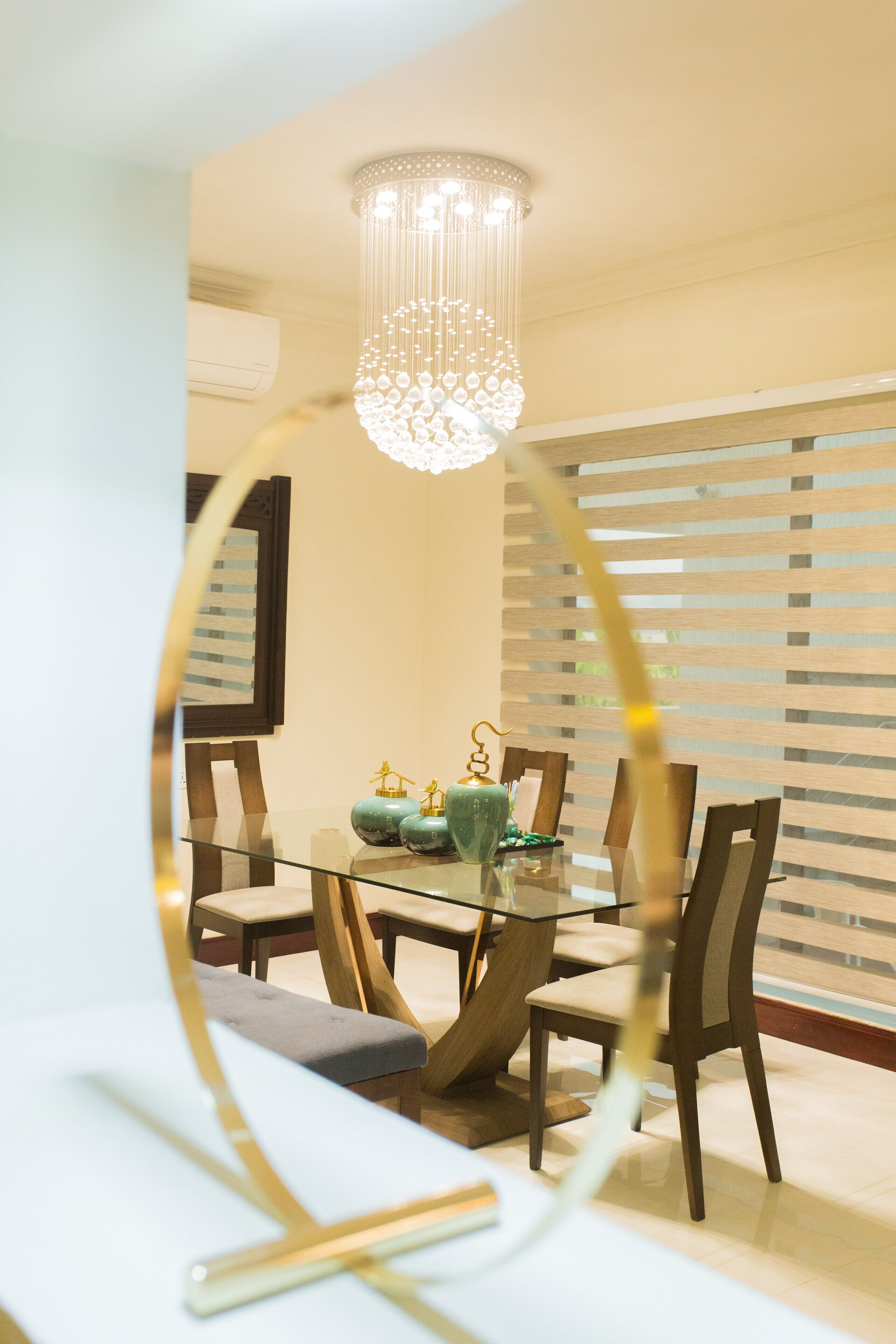 Un comedor con una mesa de vidrio, sillas de madera y una lámpara decorativa.