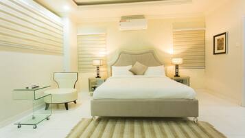 A modern bedroom with a large bed, bedside lamps, a glass cart, and a chair.