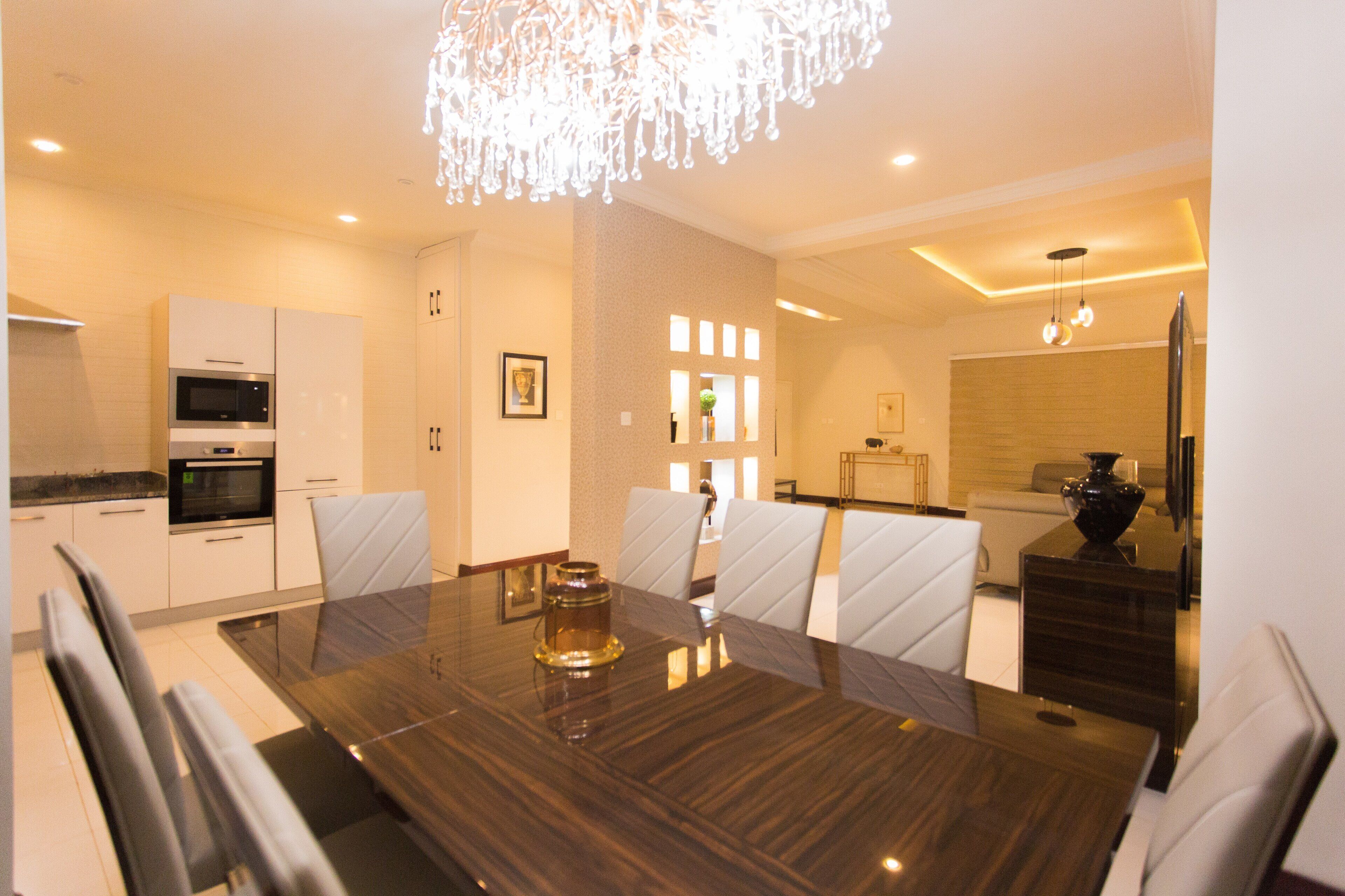 Un espace repas moderne avec une table en bois foncé, des chaises à revêtement blanc et un lustre.