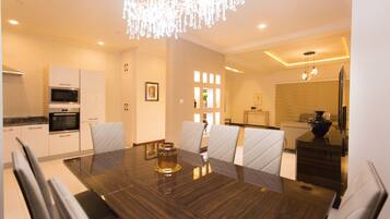A modern dining area with a dark wood table, white upholstered chairs, and a chandelier.