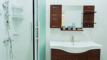 A bathroom with a glass shower enclosure, a white sink, and wooden cabinets.