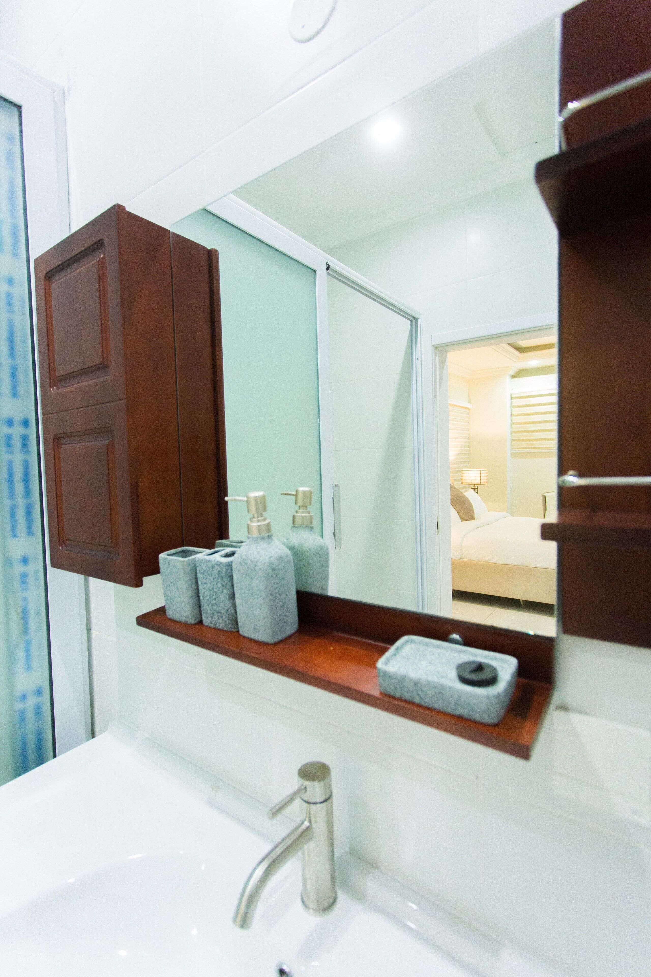 A bathroom with a white sink, a wooden cabinet, a mirror, and a shelf with toiletries.