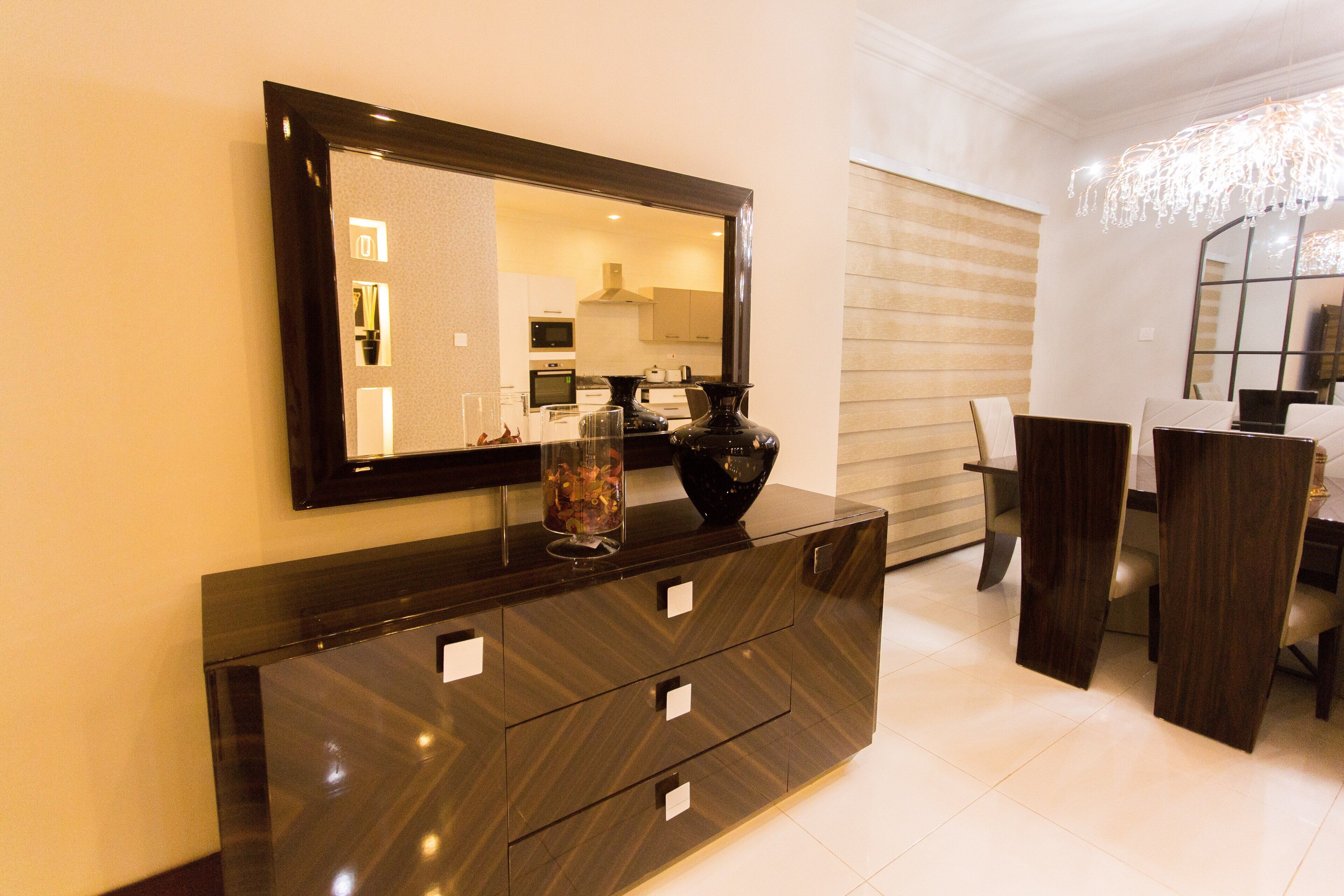 Un espace repas moderne avec une table à manger en bois foncé, des chaises et un grand miroir placé au-dessus d’une console en bois foncé dotée de tiroirs.