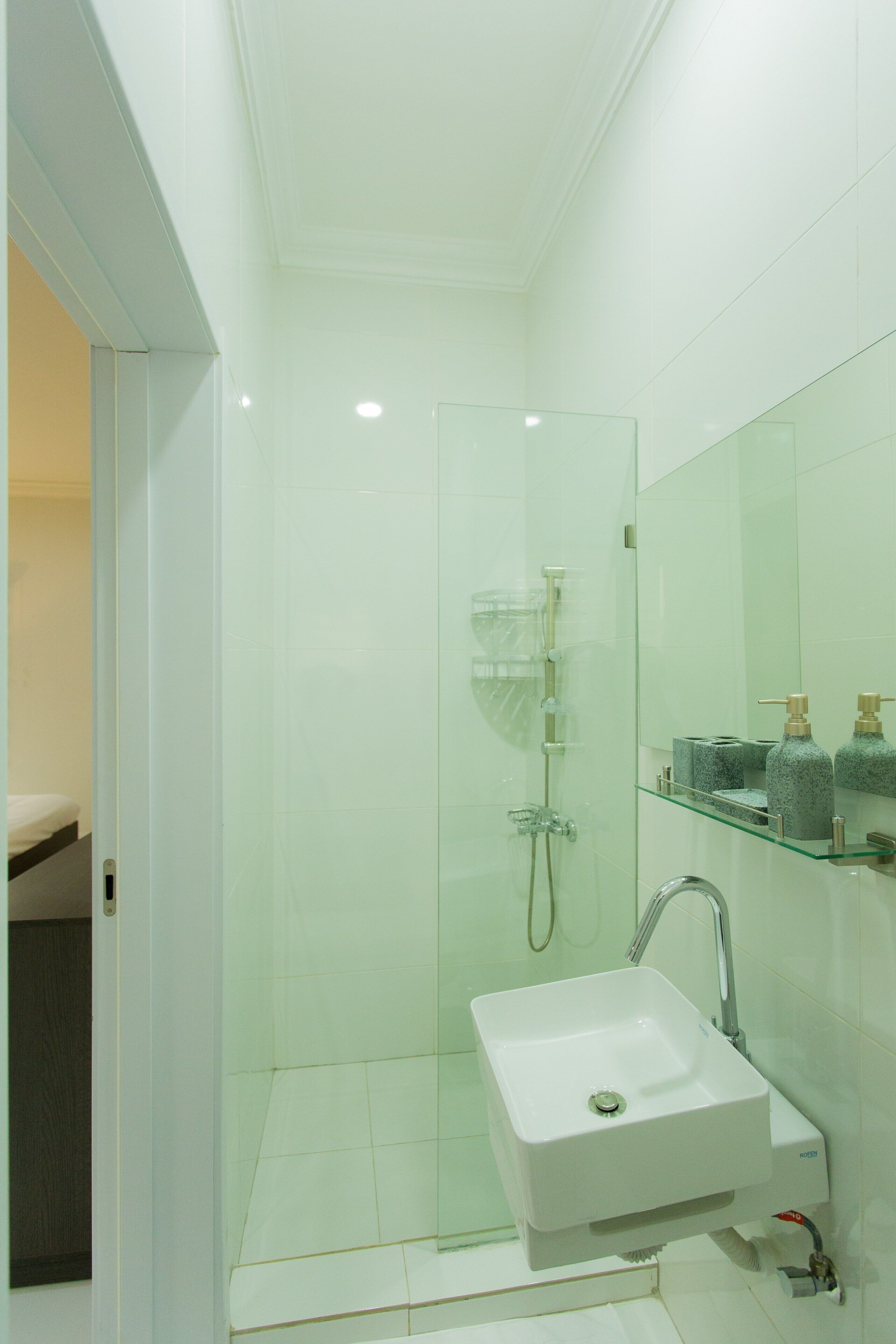 A modern bathroom with a glass-enclosed shower, a white sink, and a glass shelf with toiletries.