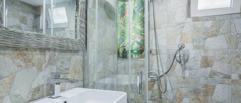 A bathroom with a glass-enclosed shower, a white sink, and a stone wall.