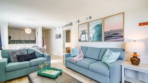 A living room with two sofas, a coffee table, and a dining area with a kitchen in the background. - Kill Devil Hills Condo w/ Beach Access On-Site! (Kill Devil Hills)