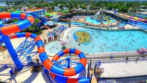 A water park with multiple slides and pools, surrounded by beach areas and umbrellas. - NEW!Pool!Hot Tub!Oceanfront! Peninsula #303 (Daytona Beach)