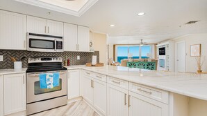 A modern kitchen with white cabinetry, a built-in microwave, and an oven. There is a view of the ocean through large windows. - NEW!Pool!Hot Tub!Oceanfront! Peninsula #303 (Daytona Beach)