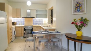 A modern kitchen with a central island, clear chairs, a dining table, and a yellow vase with flowers. - Aeri Home - At Nea Chora beach w. Parking included (Chania)