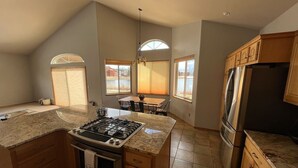 Una cocina con una isla central, estufa y refrigerador. Hay ventanas que aportan luz natural y vistas al exterior.