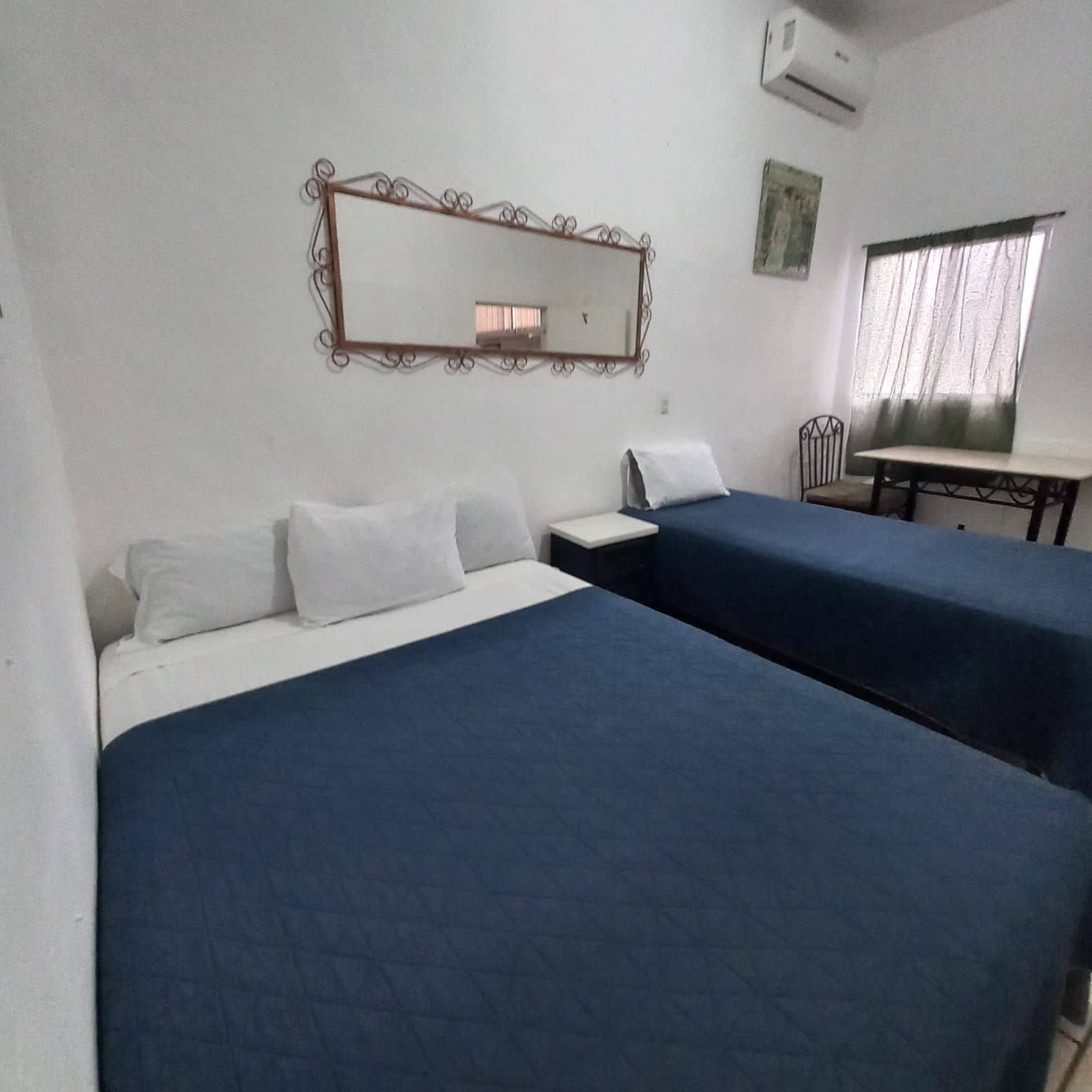 Una habitación con dos camas, un escritorio, una silla, un espejo y un equipo de aire acondicionado.