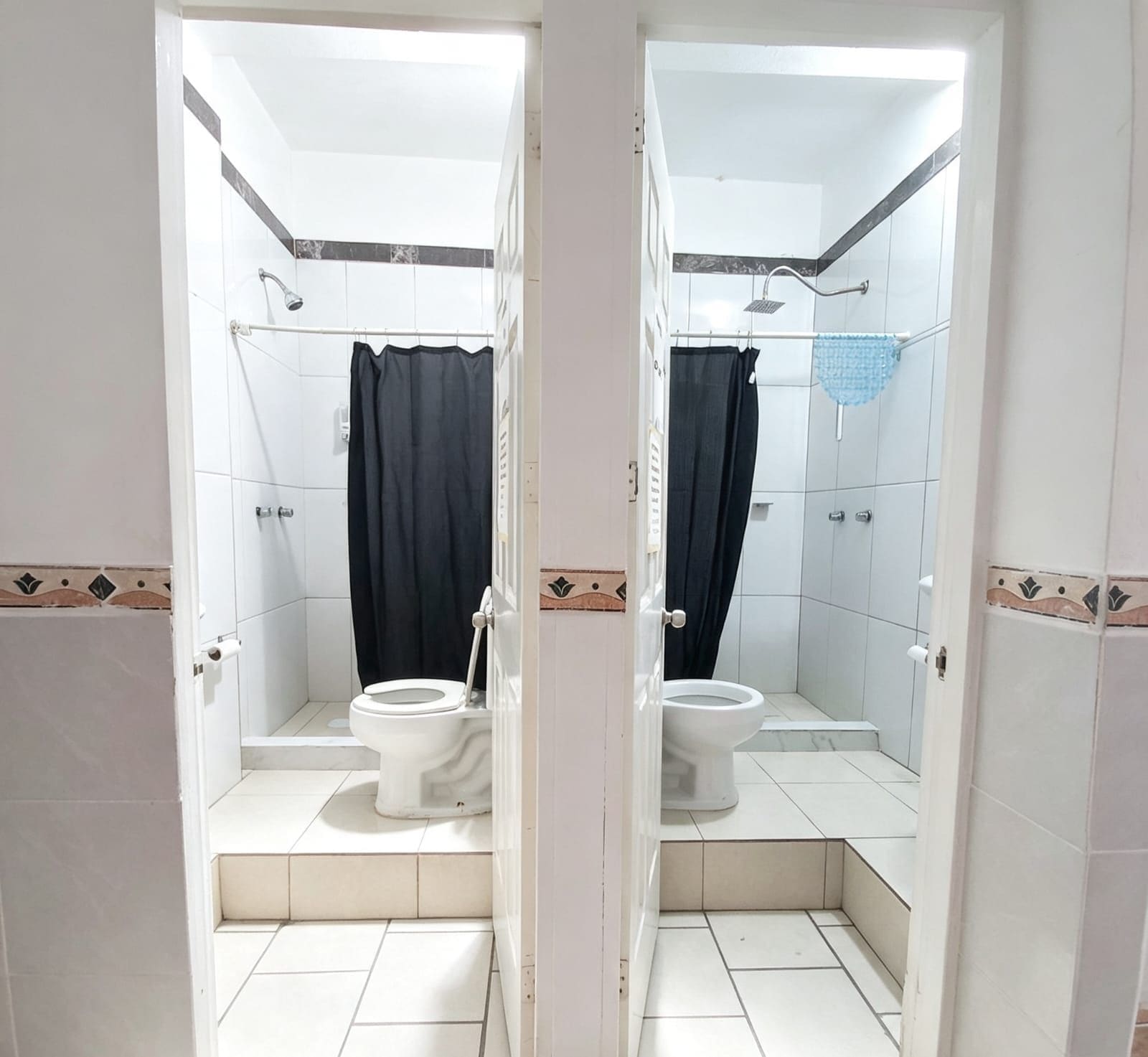 A mirrored view of a bathroom with two toilets, a shower, and a tiled floor.