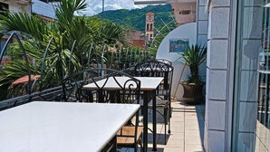 Un espace extérieur aménagé en terrasse, avec des tables et des chaises, d’où l’on peut admirer un beffroi et, au loin, une montagne.