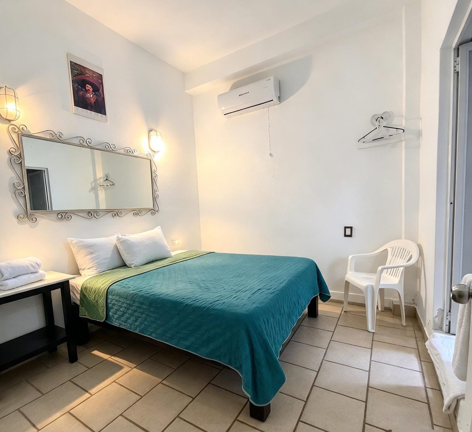 A bedroom with a bed, a bedside table, a mirror, an air conditioning unit, and a chair.