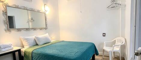 A bedroom with a bed, a bedside table, a mirror, an air conditioning unit, and a chair.