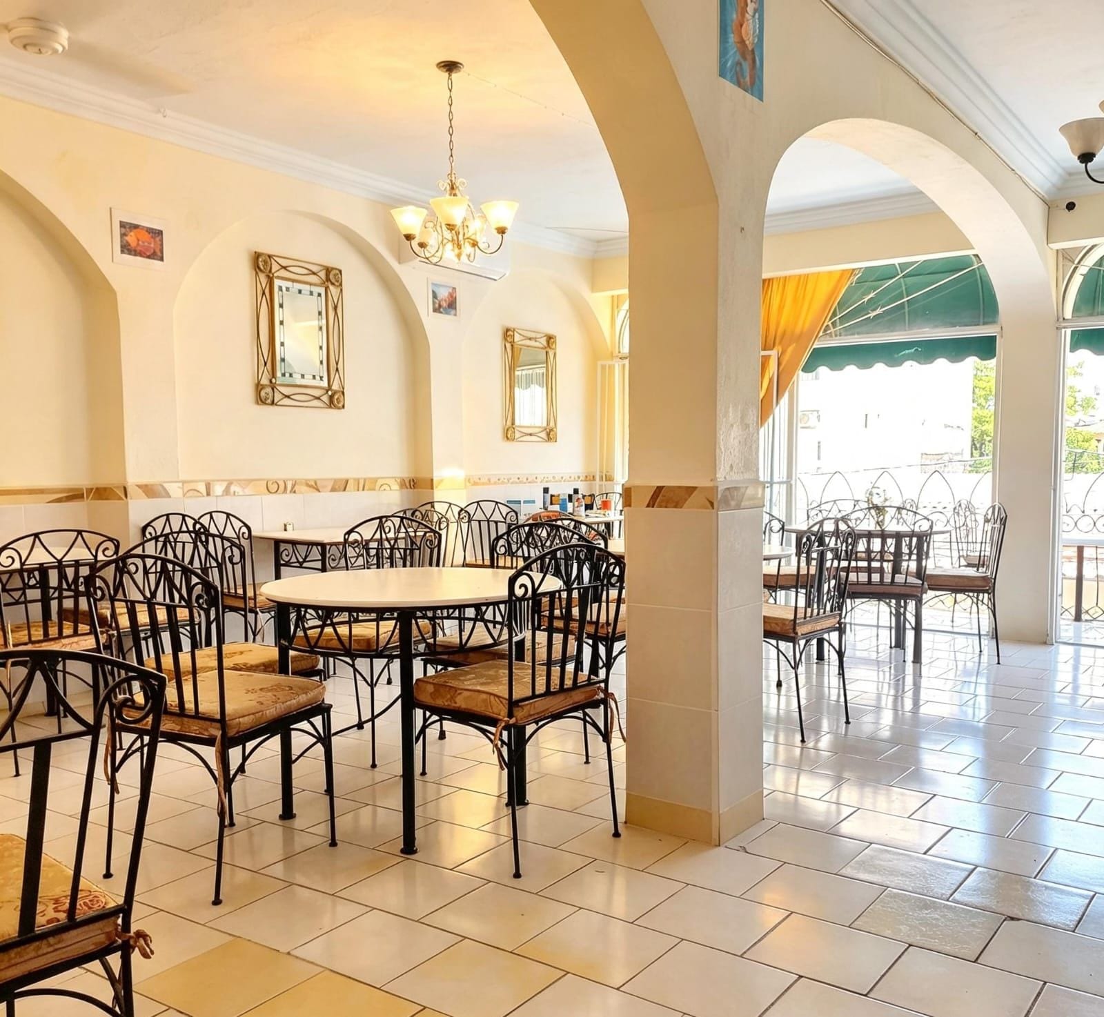 Un restaurant avec des tables et des chaises rondes, un lustre et une vue sur une terrasse couverte.