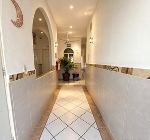 Un couloir avec un sol carrelé, un ventilateur de plafond, des appliques murales et une plante en pot.