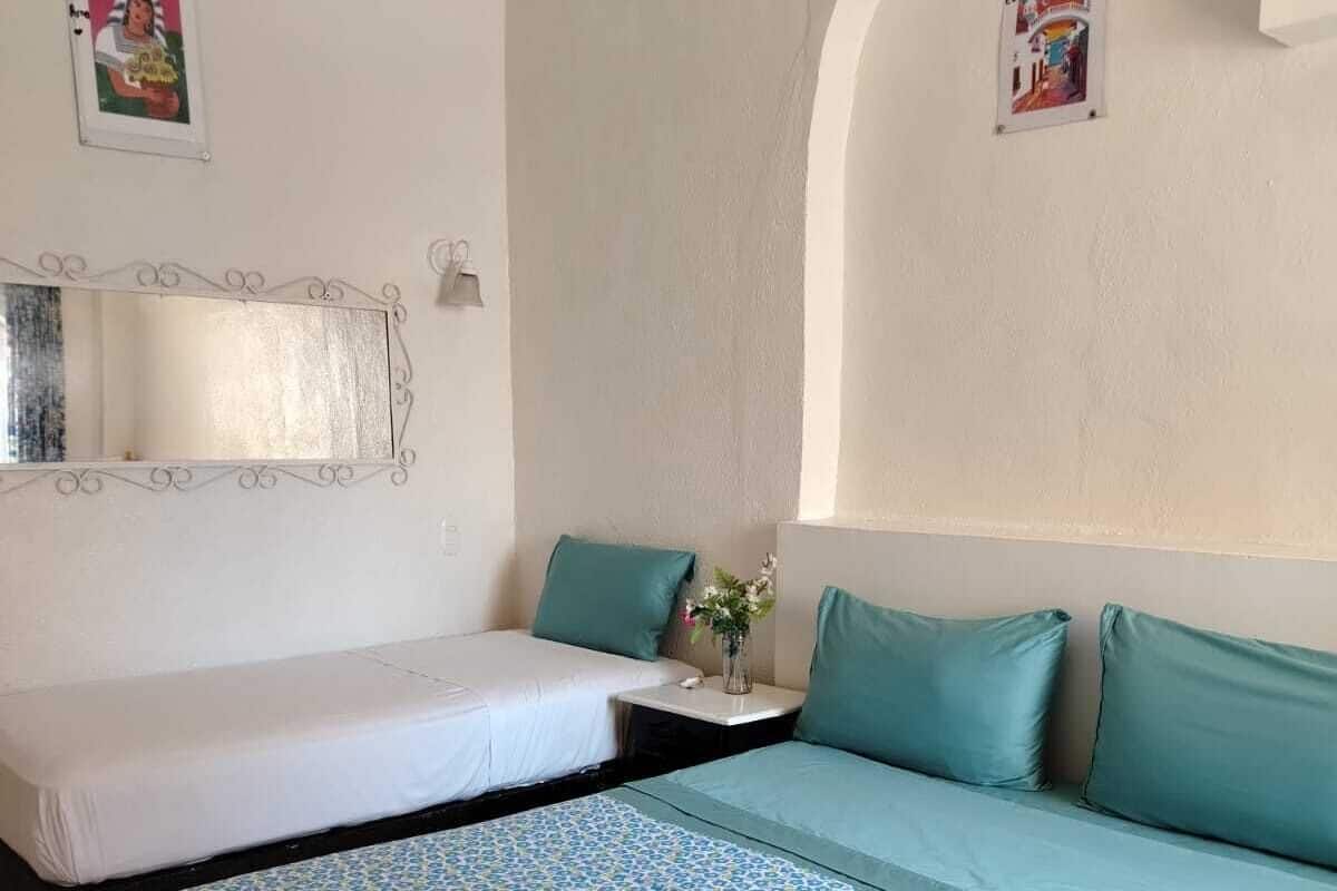 Une pièce avec un lit, une petite table sur laquelle se trouve un vase, et un miroir au mur.