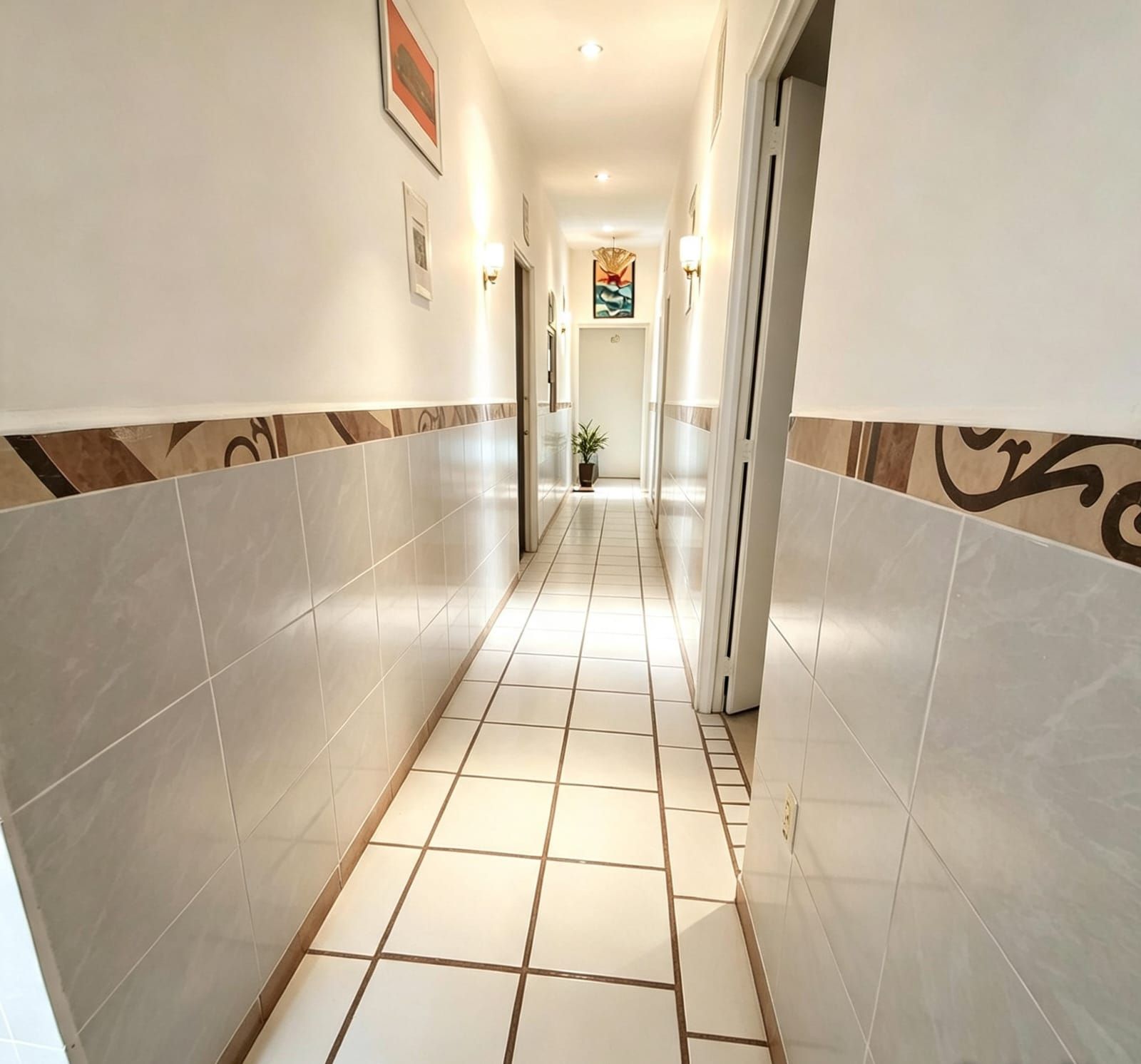 A hotel hallway with tiled flooring, a potted plant, and framed artwork on the walls.