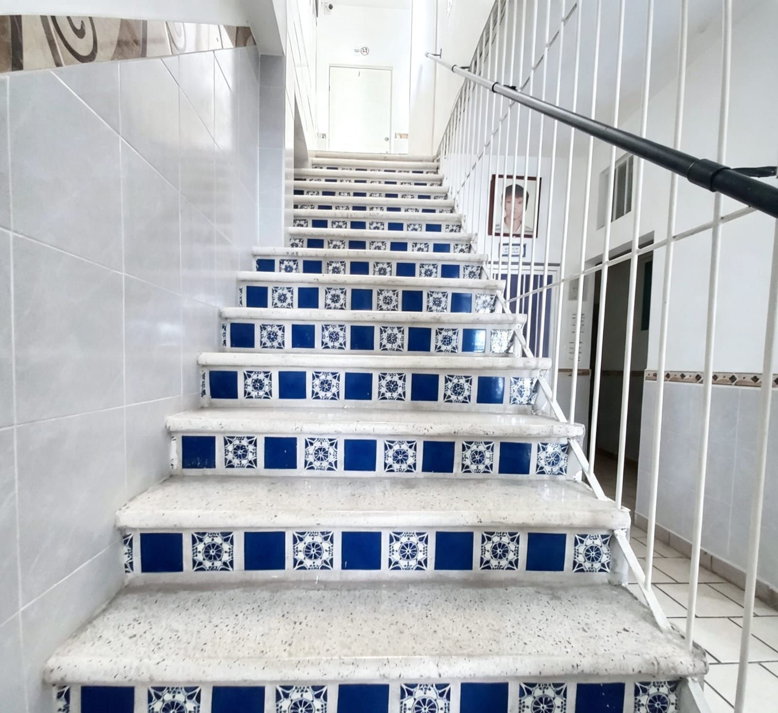 A staircase with white and blue patterned tiles, metal railings, and a handrail.