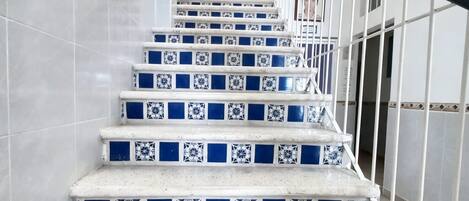 Una escalera con baldosas blancas y azules de diseño, barandales de metal y pasamanos.