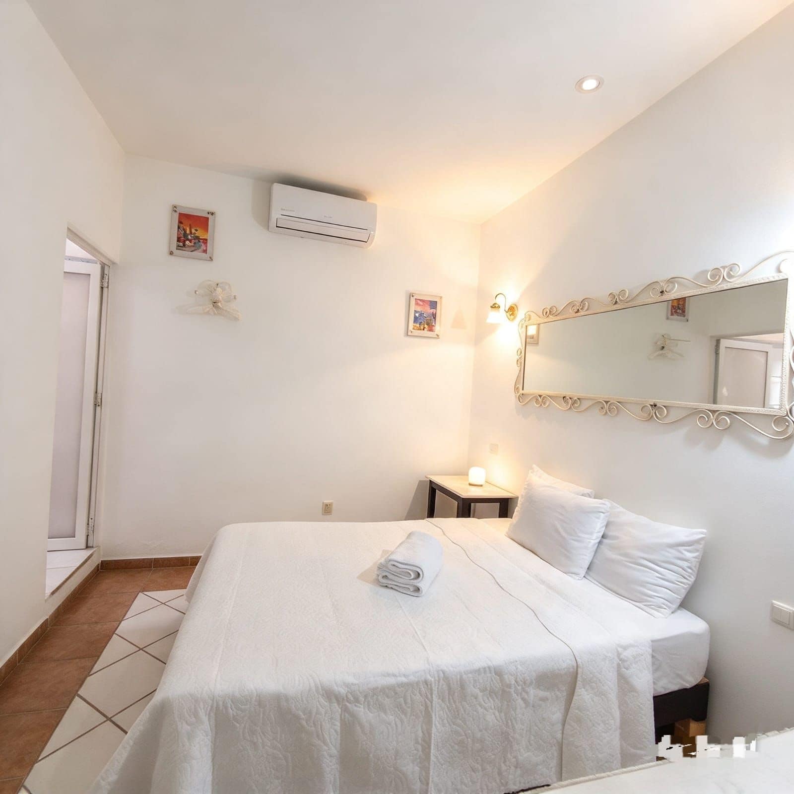 Une chambre d’hôtel comprenant un lit, une table de chevet avec une lampe, un climatiseur fixé au mur et un miroir avec un cadre décoratif.