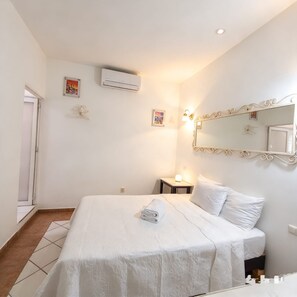 Une chambre d’hôtel comprenant un lit, une table de chevet avec une lampe, un climatiseur fixé au mur et un miroir avec un cadre décoratif.