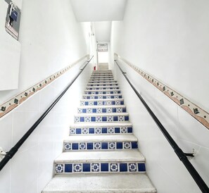 Eine Treppe mit weißen Wänden und blauen, gemusterten Fliesen, die zu einem Zwischenpodest mit einem Schild führt.