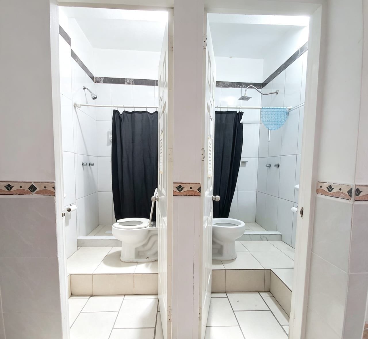 A bathroom with two toilets, a shower, and a mirror.