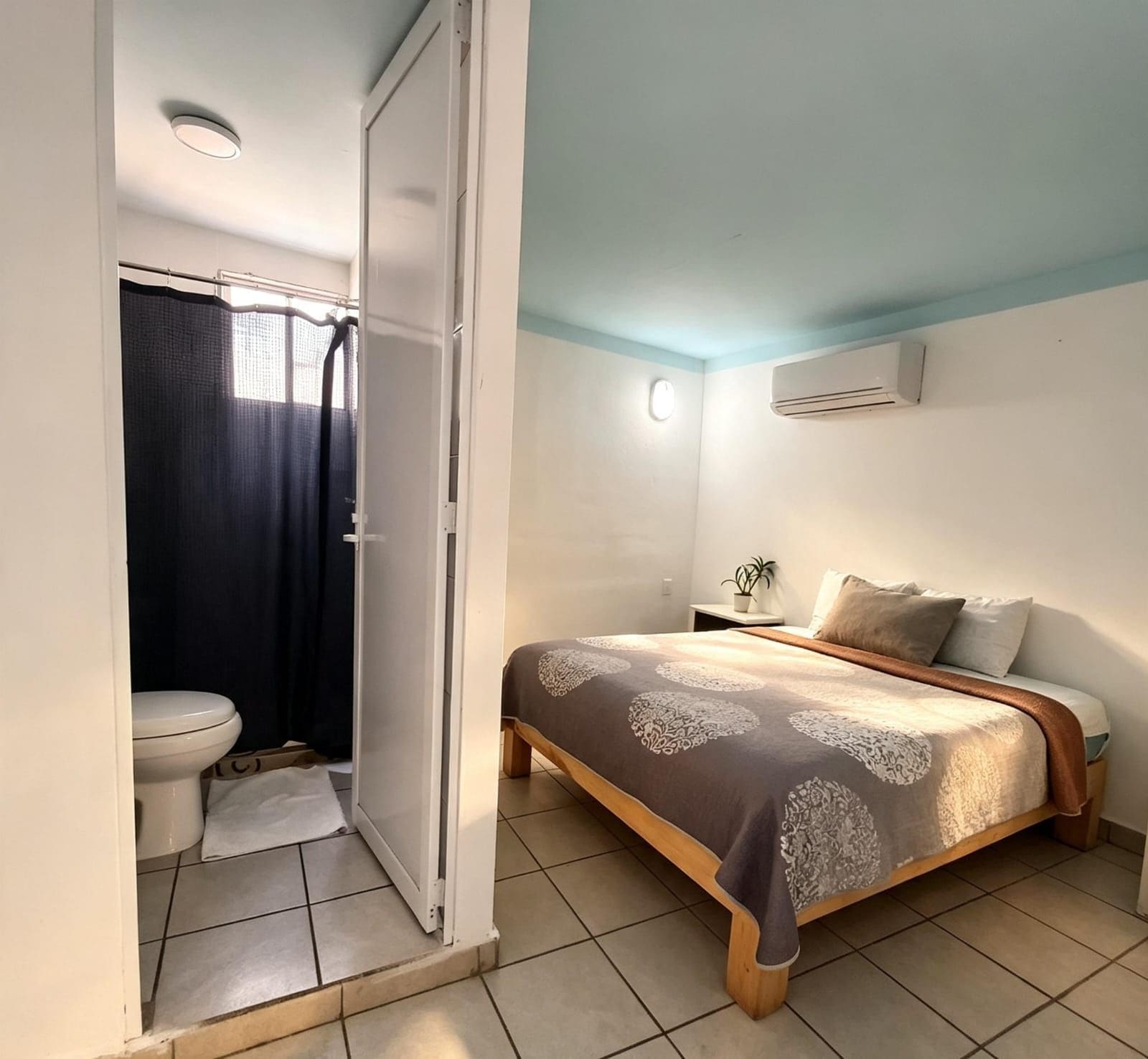 Un dormitorio con cama, mesita de noche, ventana y baño con inodoro y ducha.