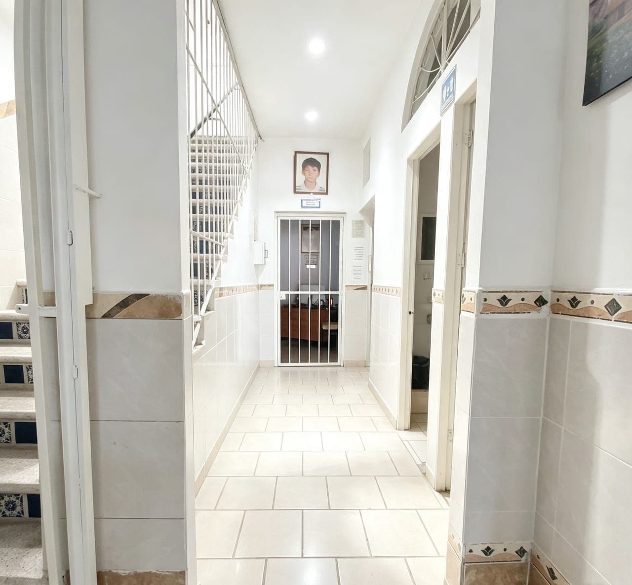 A hallway with a tiled floor, white walls, and a metal gate.