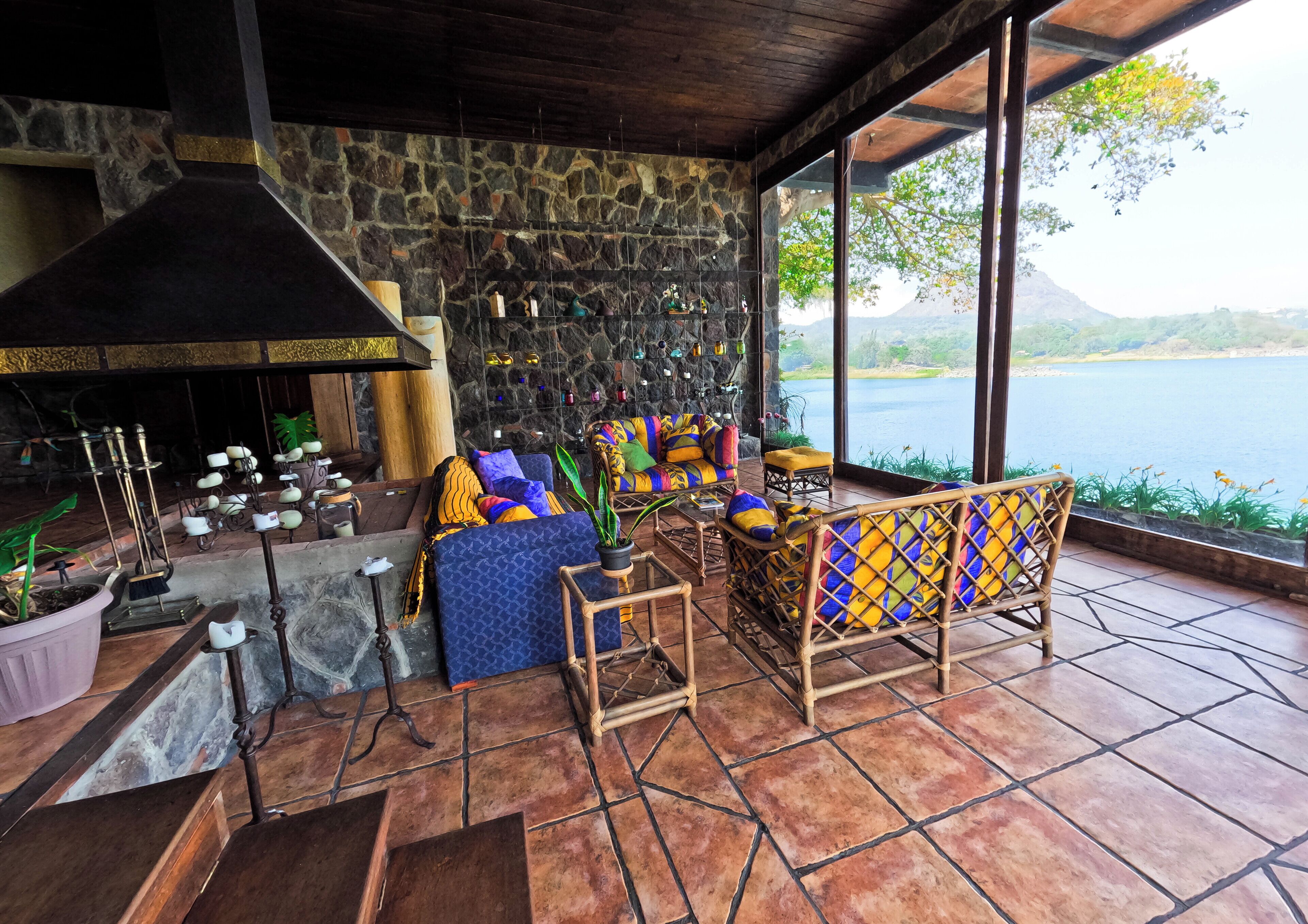 A cozy outdoor seating area with stone walls, a fireplace, and a view of a lake.